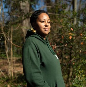 A woman in a green sweatshirt stands in an urban garden.