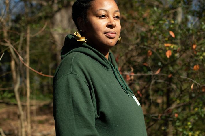 A woman in a green sweatshirt stands in an urban garden.