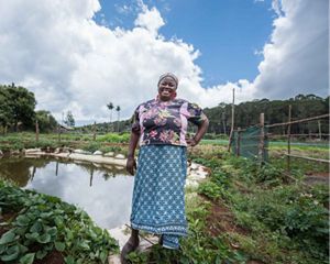 A farmer stands in front of her rainwater harvesting pan.