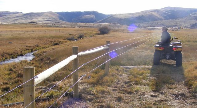 A rancher on an ATV surveys his wildlife friendly fence. 