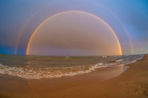 A rainbow over Lake Huron as waves flow onto the sandy beach.