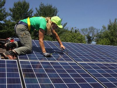 A worker installs solar panels on a roof.