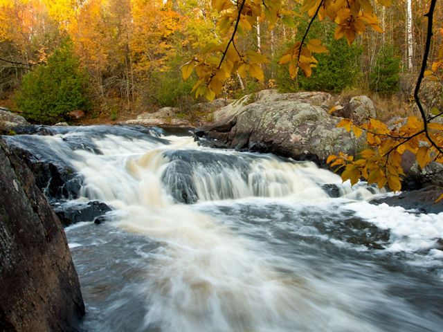 A waterfall is framed by yellow leaves of trees in autumn.
