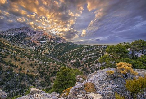 Landscape view of mountains with rocks in foreground and sunlit clouds overhead.