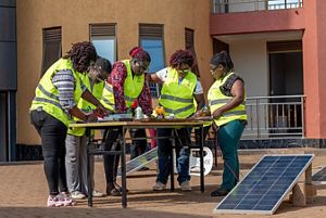 A group of young women use tools to assemble solar panels.