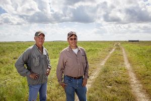 Two TNC employees wearing baseball caps stand in a never-ending expanse of green prairie.