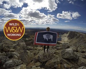 Girl with Wyoming state flag stands on mountain under cloudy blue skies.