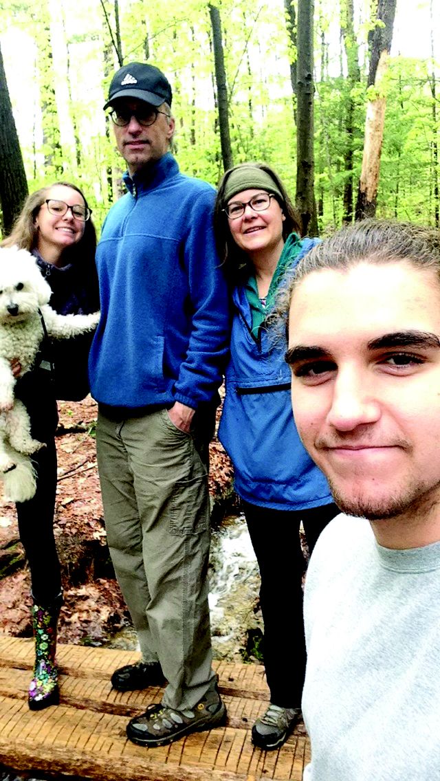 A selfie of a young man with his parents, sister and dog posing in the background.