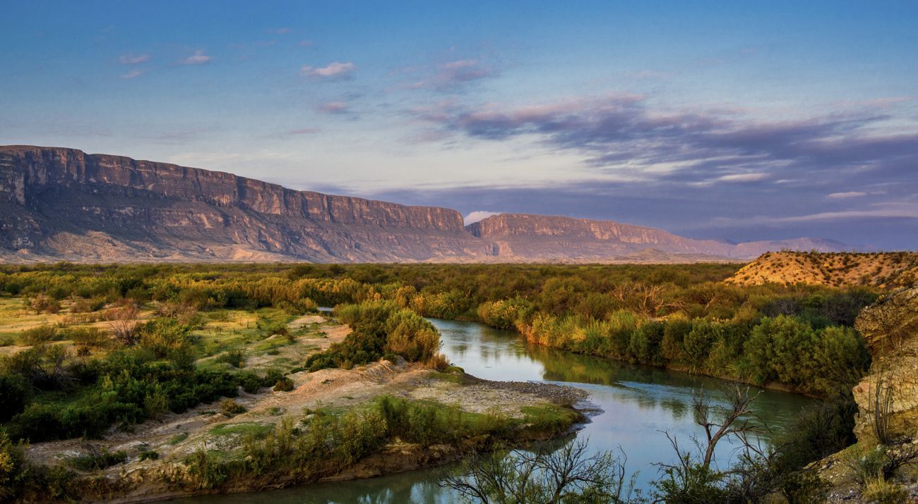 a view of the rio grande and a canyon in the background against a sunset sky.