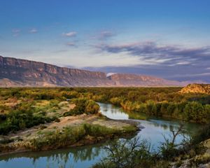 view of the rio grande and a canyon in the background against a sunset sky.