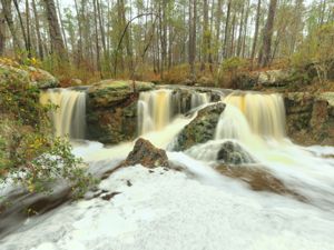 A rocky waterfall with water rushing in a forest landscape.