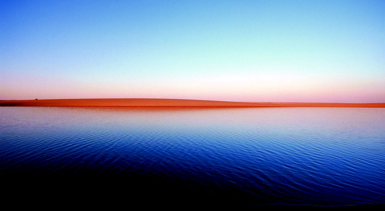 Photo of Egyptian desert landscape, with sky above, a line of sand along the horizon, and water below.