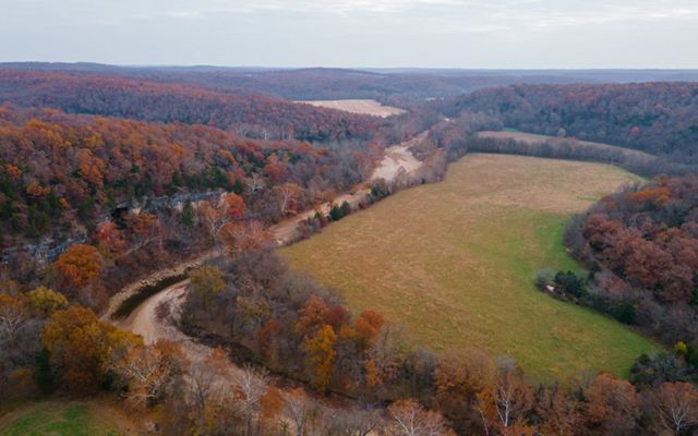 Aerial view of a winding creek running through a forested property on a fall day.