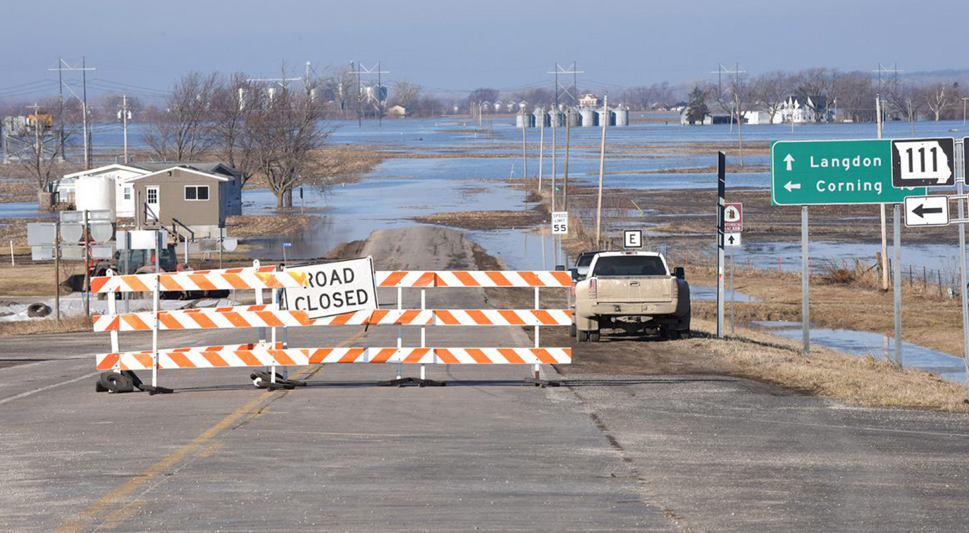 A road closed sign stretches across a flooded road. 