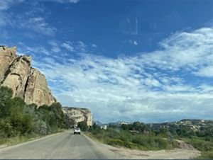 A sandstone cliff rises next to a two-lane road.