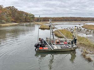 Two people park a boat next to a narrow wetland.