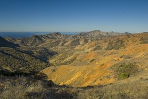 Rugged, semi-arid terrain in the foreground with a view of the open ocean in the distance.