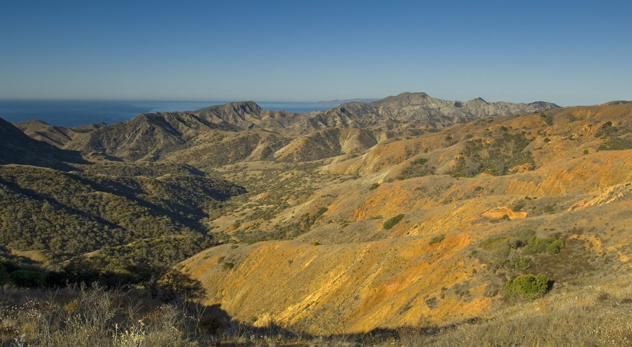 Rugged, semi-arid terrain in the foreground with a view of the open ocean in the distance.