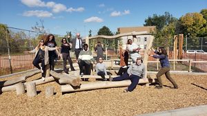 Eleven people pose in different ways around a natural feature at a playground.