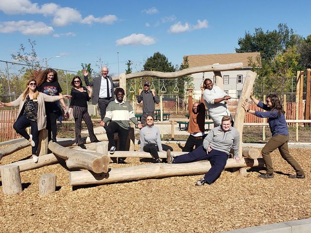 Eleven people pose in different ways around a natural feature at a playground.