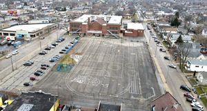 An overhead drone image of a large concrete schoolyard with a brick school in the background.