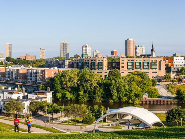 Two people walk on a path in a park with the Milwaukee skyline in the background.