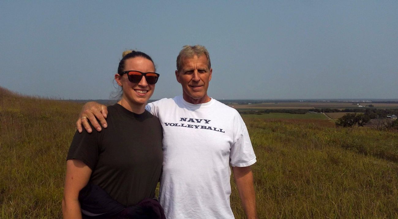 A young woman with her father who has his arm around her standing in wide open prairie.