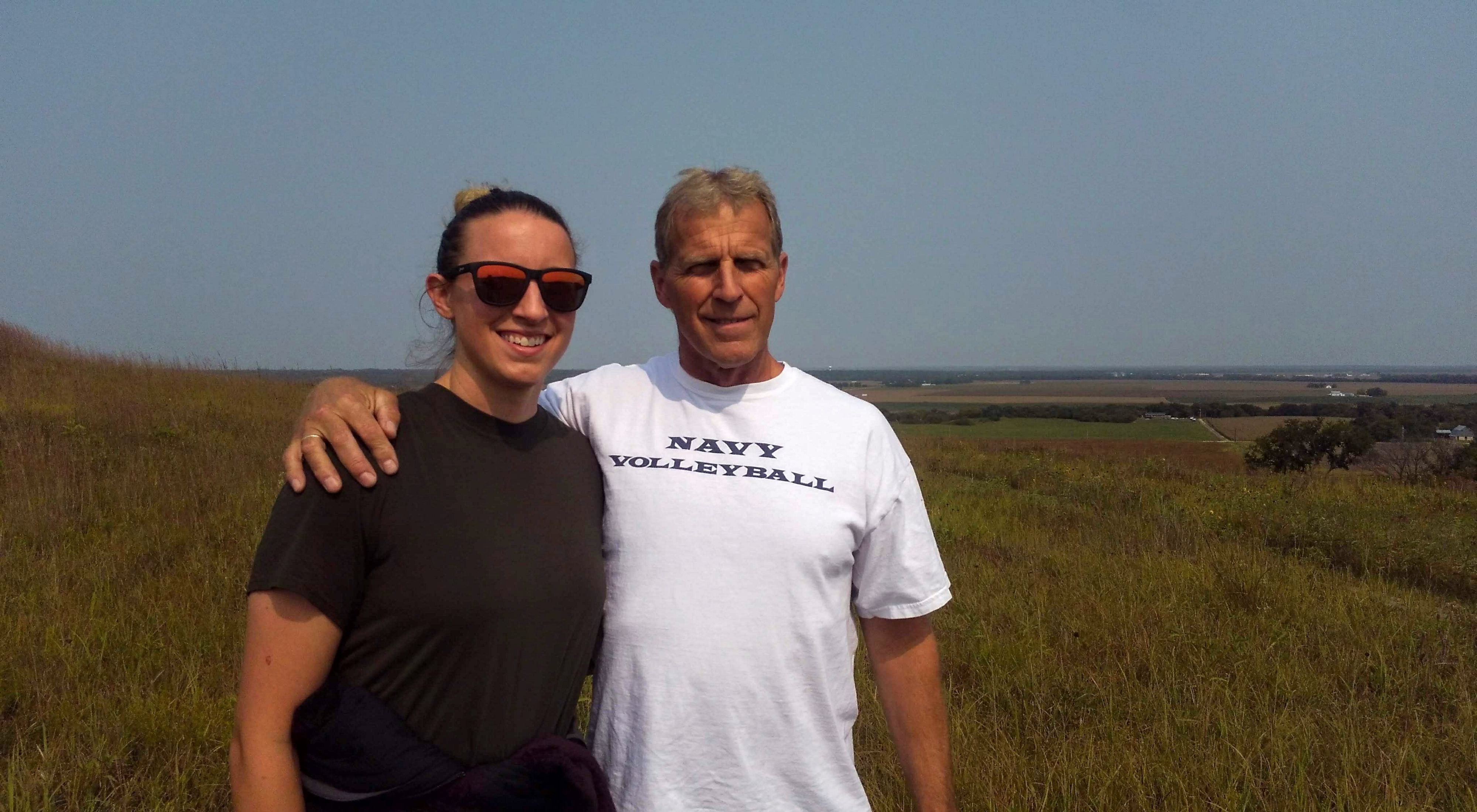 A young woman with her father who has his arm around her standing in wide open prairie.