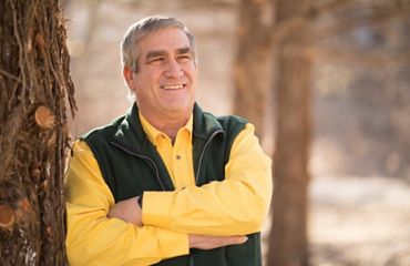 Smiling man with crossed arms leans against a tree.