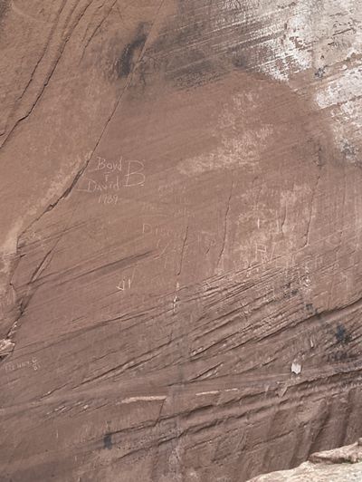 Graffiti is scratched into the surface of a sandstone cliff face.