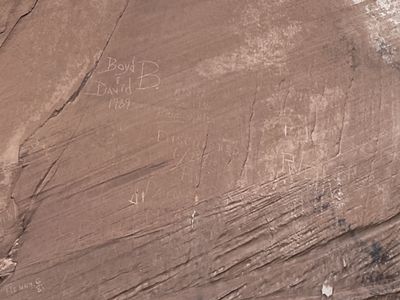 Graffiti is scratched into the surface of a sandstone cliff face.