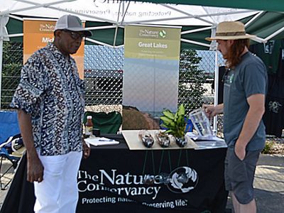 TNC staff speaking with Sacred Heart parishioner in front of a table with a black tablecloth with a white TNC logo on it.
