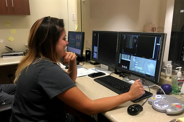 A technician smiles as she sits at a computer monitor.