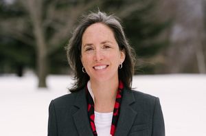 A backpacker viewed from behind, walking on the side of a boulder-strewn hill with an ice-filled valley in the distance.