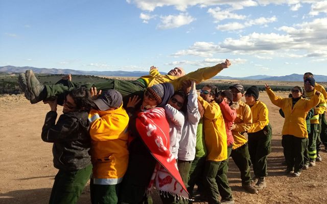 A dozen wildland fire workers engage in a trust-building exercise by carrying a man over their heads.