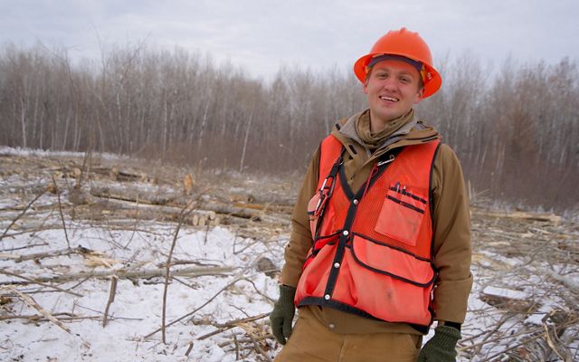 A smiling forester wearing an orange vest and hardhat. 