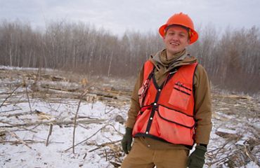A smiling forester wearing an orange vest and hardhat.