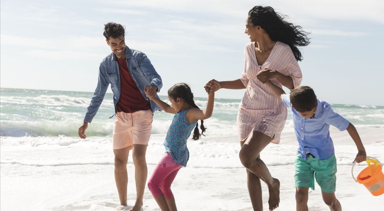 A family holding hand running along the beach.