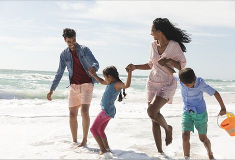 A family holding hands running along the beach.