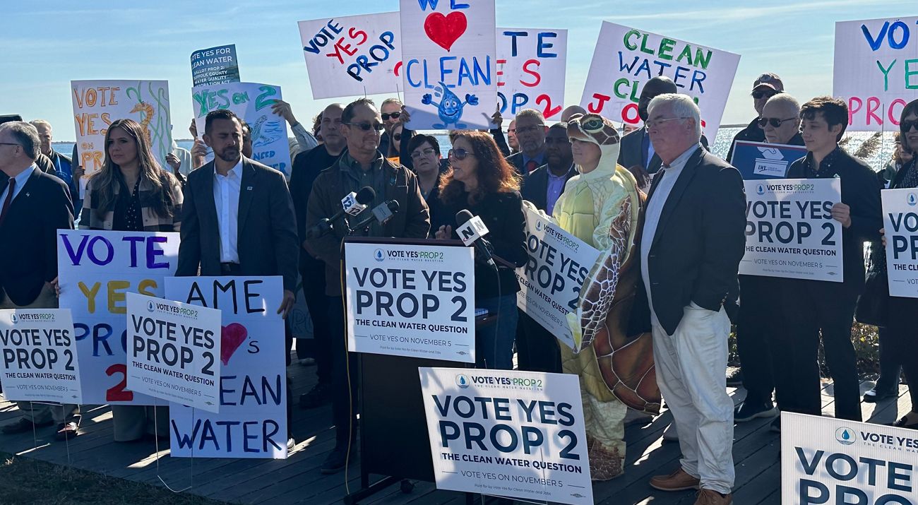 A group of people rallying with "Prop 2" and "We Love Clean Water" signs.
