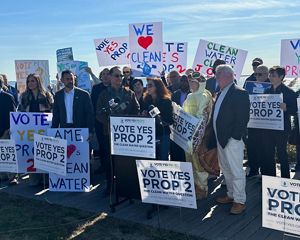 A group of people rallying with "Prop 2" and "We love clean water" signs.