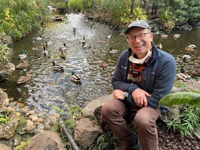 mike schaefer sitting by a pond filled with ducks.