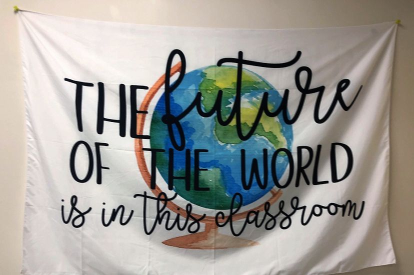  Una pancarta de tela blanca con el dibujo de un globo terráqueo dice: «El futuro del mundo está en este salón de clase».