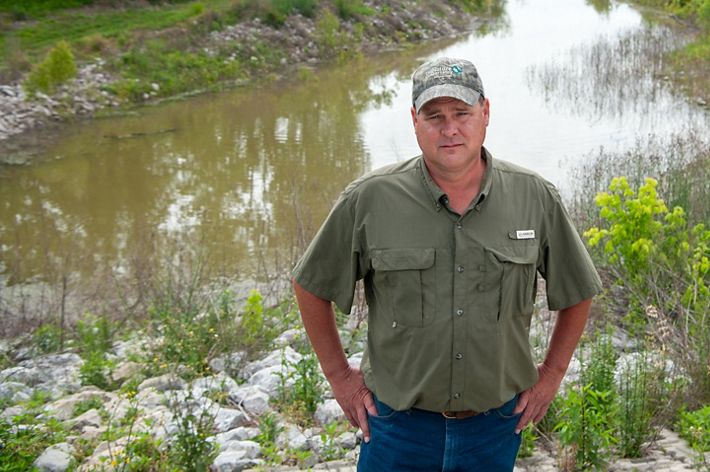 A man wearing a hat stands in front of a wetland.