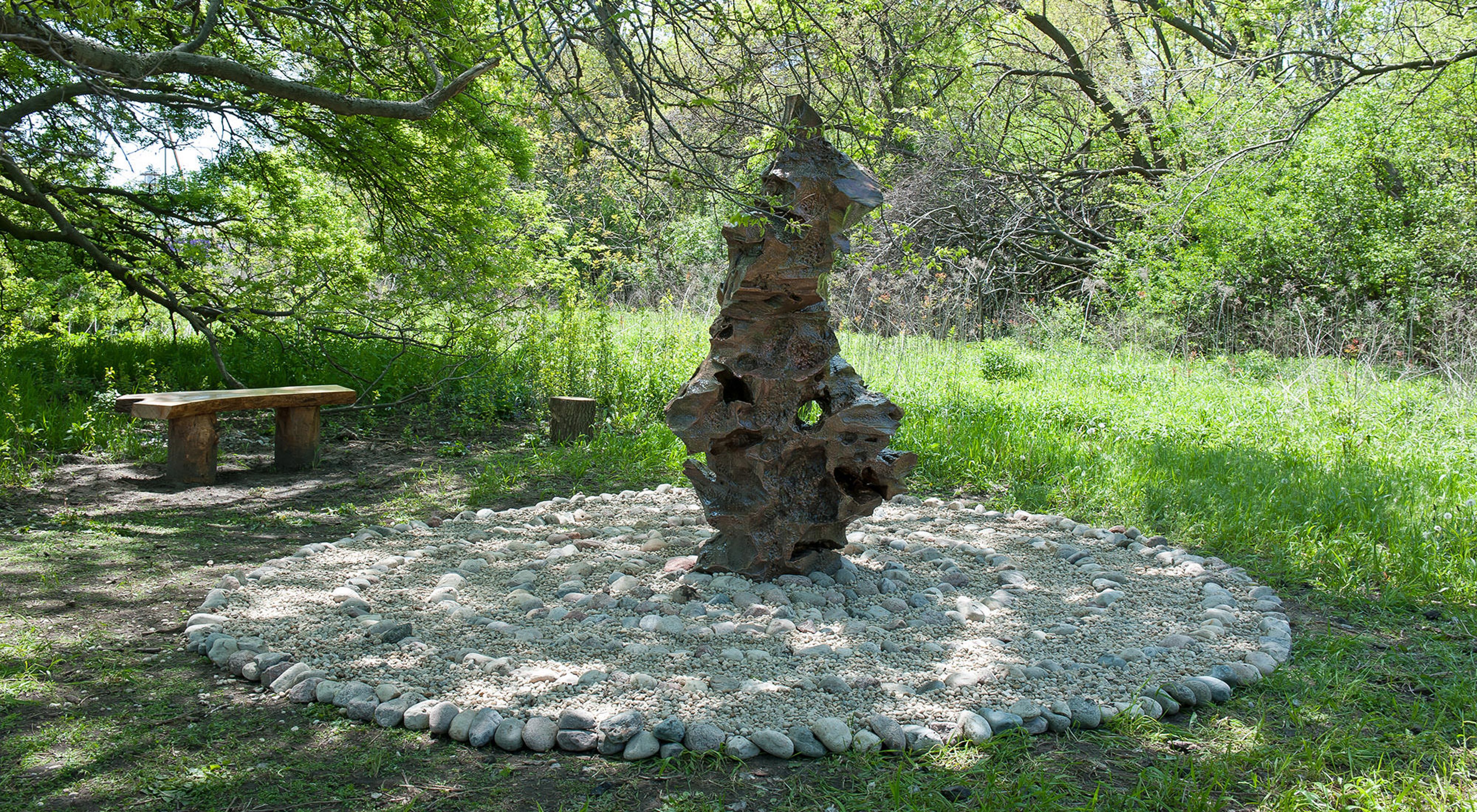 A stone sculpture with a bench in a gathering space along the Burnham Wildlife Corridor. 