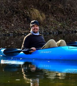 Man in blue kayak on calm creek.