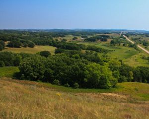 View of a hilly prairie landscape with bunches of trees beside a lake.