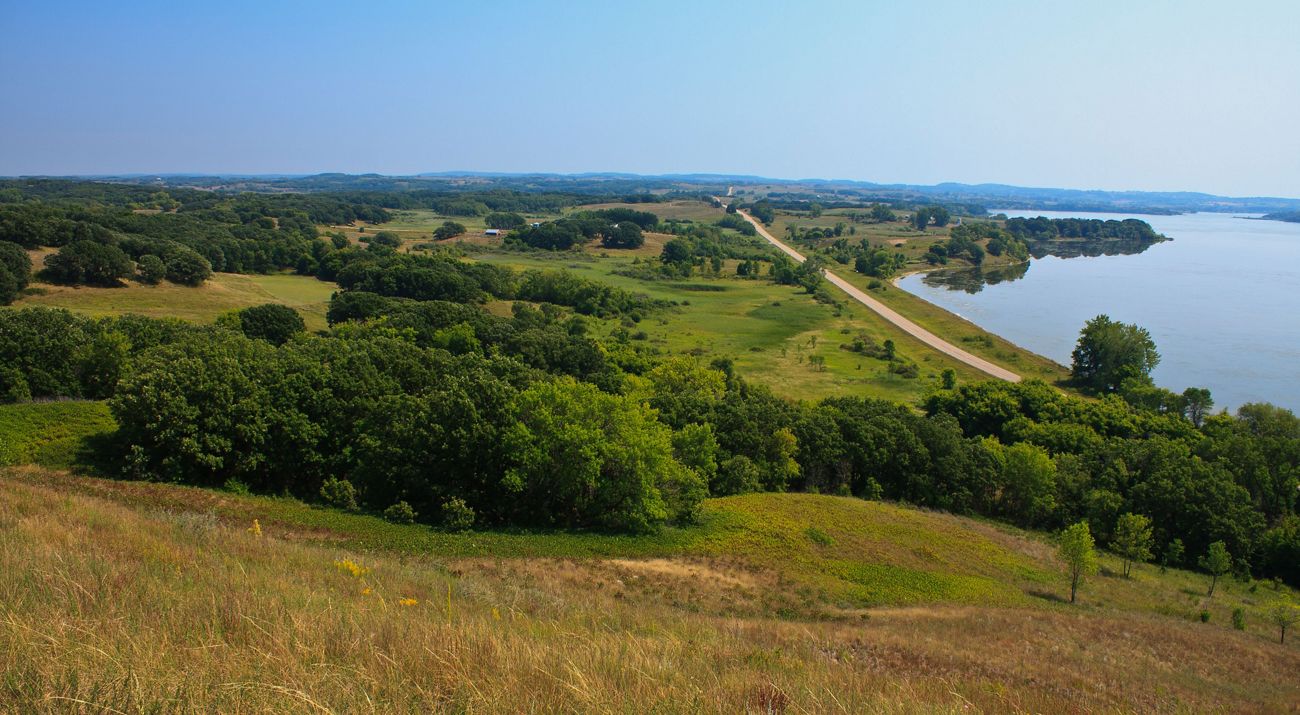 View of a hilly prairie landscape with bunches of trees beside a lake.