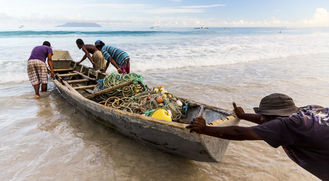 men pushing a small wooden boat filled with fishing nets.