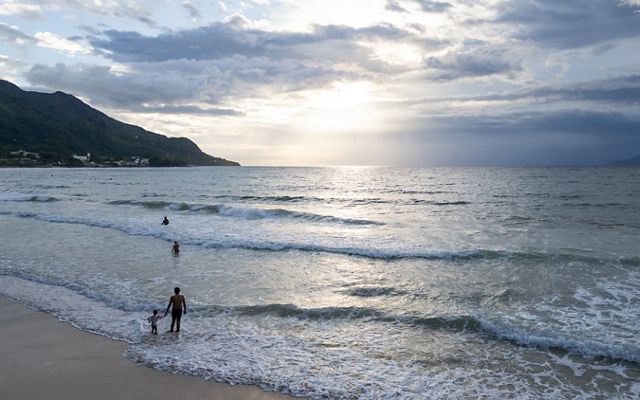 Wide view of water lapping on a beach as people wade in the shallow part of the water.